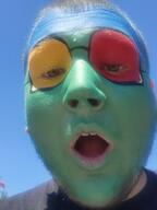 blue_skin brown_hair carnival colorful ear face_paint glasses green_skin hair irl open_mouth red_skin soyjak stubble variant:unknown white_skin yellow_skin yellow_teeth // 2208x2944 // 1.4MB