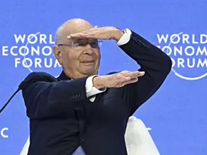 klaus schwab, bald, chair, closed mouth, clothed, clothes, fat, glasses, irl background, looking to the right